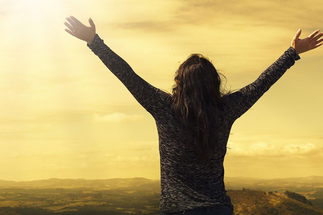 Ansicht von hinten auf eine junge Frau, die die Arme über den Kopf hält und tief einatmet